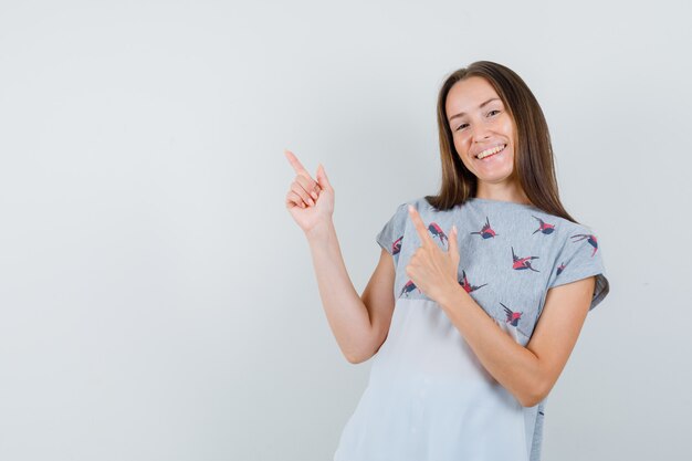 Jonge vrouw pistool gebaar in t-shirt tonen en gelukkig kijken. vooraanzicht.