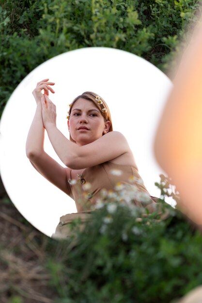 Jonge vrouw poseren buiten in een veld met een ronde spiegel