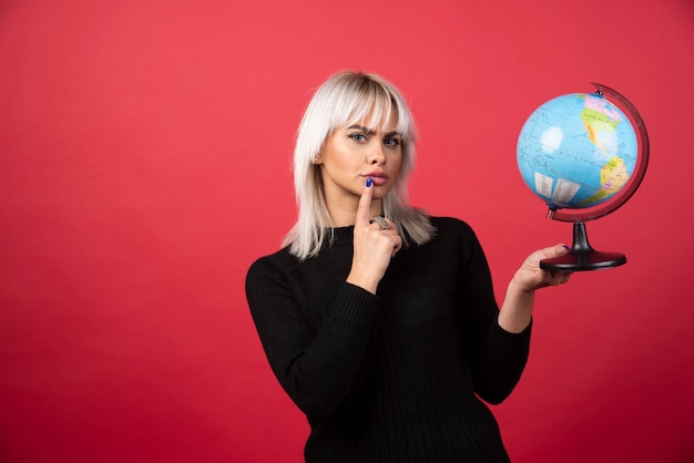 Jonge vrouw poseren met een wereldbol op een rode achtergrond. Hoge kwaliteit foto