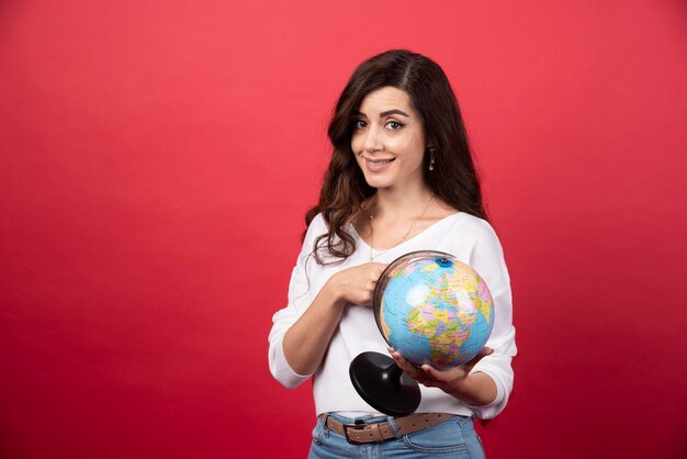 Jonge vrouw poseren met globe op rode achtergrond. Hoge kwaliteit foto