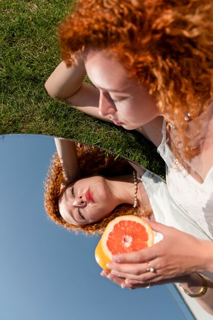 Gratis foto jonge vrouw poseren met grapefruit in de spiegel op gras