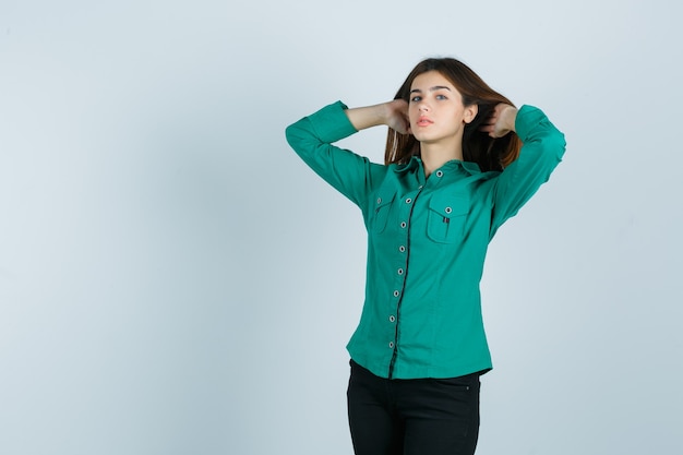 Jonge vrouw poseren met haar kastanjebruin haar in groen shirt, broek en op zoek verleidelijk. vooraanzicht.