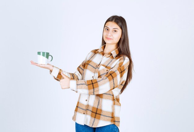 jonge vrouw poseren met kopje koffie op witte muur.