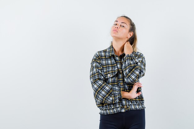 Jonge vrouw poseren terwijl hand op nek in shirt, korte broek en op zoek naar elegant, vooraanzicht.