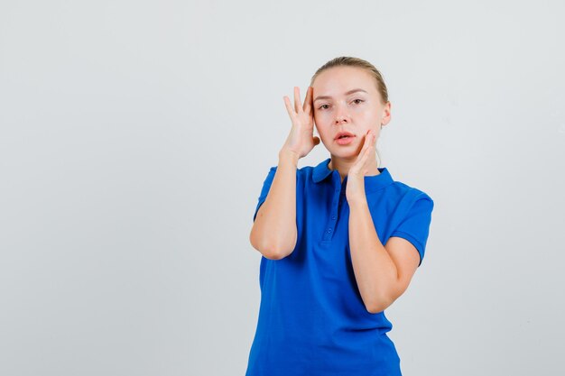 Jonge vrouw poseren tijdens het kijken in blauw t-shirt en aantrekkelijk kijken