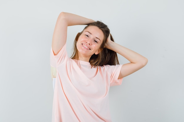 Jonge vrouw poseren tijdens het regelen van haar haren in roze t-shirt en ziet er prachtig uit.
