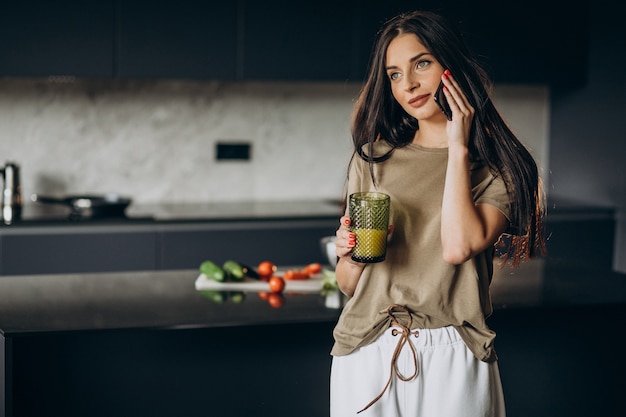 Jonge vrouw sap drinken en telefoon gebruiken in de keuken