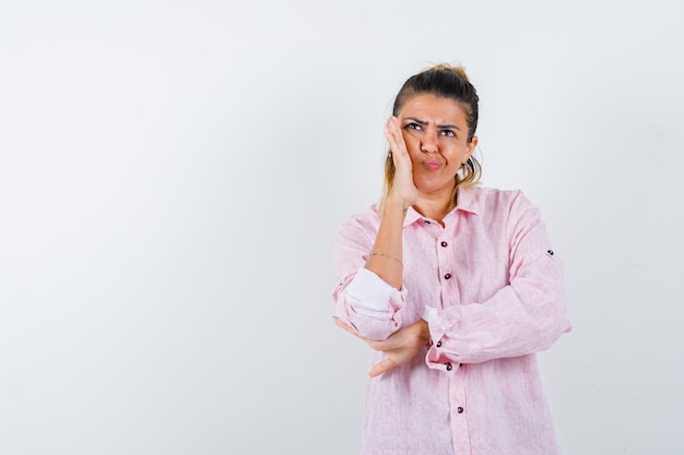 Jonge vrouw staande in denken poseren in roze shirt en besluiteloos op zoek