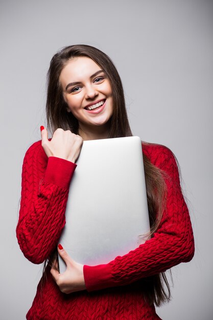 Jonge vrouw staande te houden laptop. Gelukkig jong meisje met behulp van haar laptop, geïsoleerd op een witte muur.