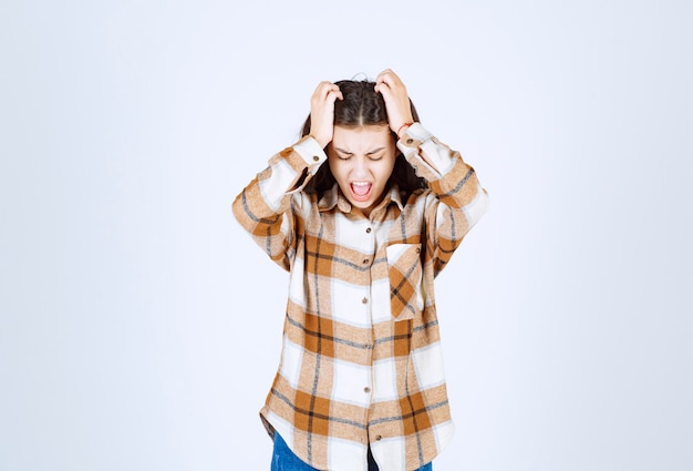 Gratis foto jonge vrouw staat en houdt haar hoofd op een witte muur.