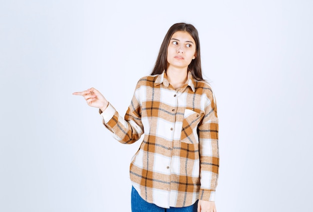 jonge vrouw staat en wijst naar ergens op de witte muur.