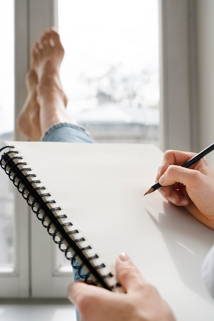 Jonge vrouw tekening thuis in de buurt van het raam