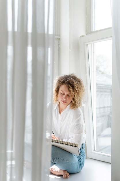 Jonge vrouw tekening thuis in de buurt van het raam