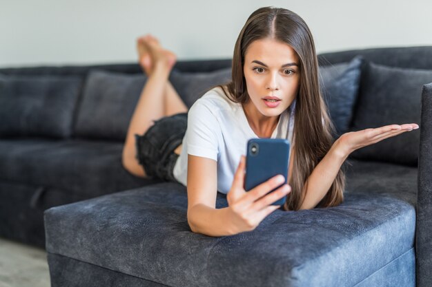 Jonge vrouw telefoon gebruiker met video-oproep. Jonge vrouw in het toevallige liggen op laag, gebruikend smartphone en glimlachend bij het scherm.