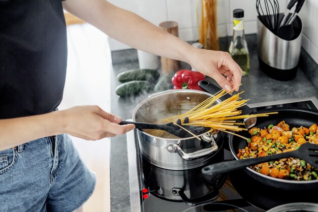 Jonge vrouw thuis koken van verse spaghetti pasta met groenten.