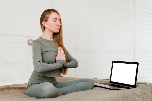 Jonge vrouw thuis mediteren met laptop naast