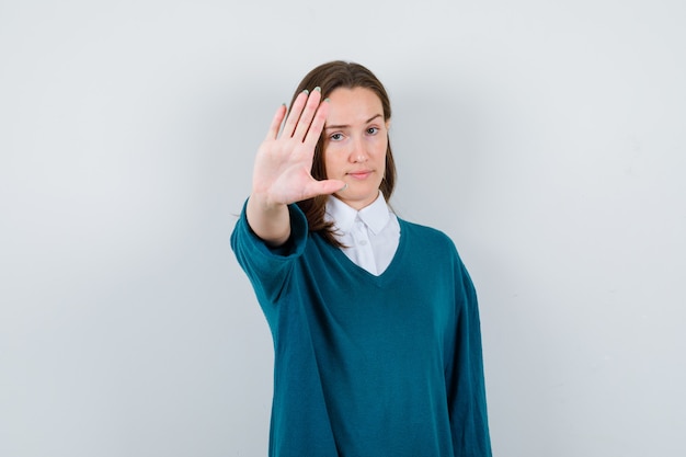 Jonge vrouw toont stopgebaar in trui over shirt en ziet er serieus uit. vooraanzicht.