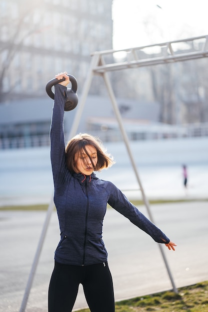 Gratis foto jonge vrouw trainen met een kettlebell buiten in het stadion