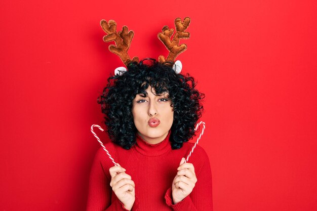 Jonge vrouw uit het Midden-Oosten die schattige kerstrendierhoorns draagt, kijkend naar de camera die een kus blaast die mooi en sexy is. liefde uitdrukking.