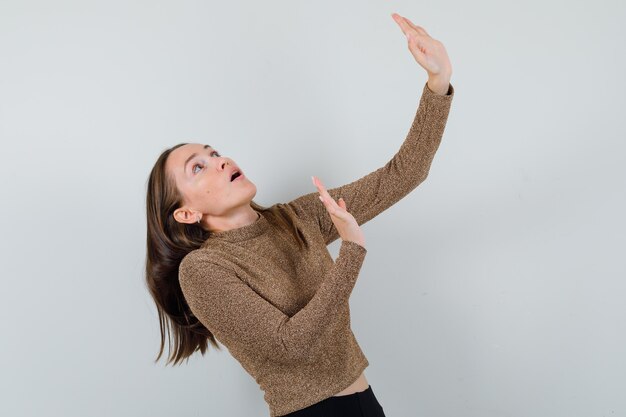 Gratis foto jonge vrouw verdedigen tegen iets in gouden blouse en bang kijken.​