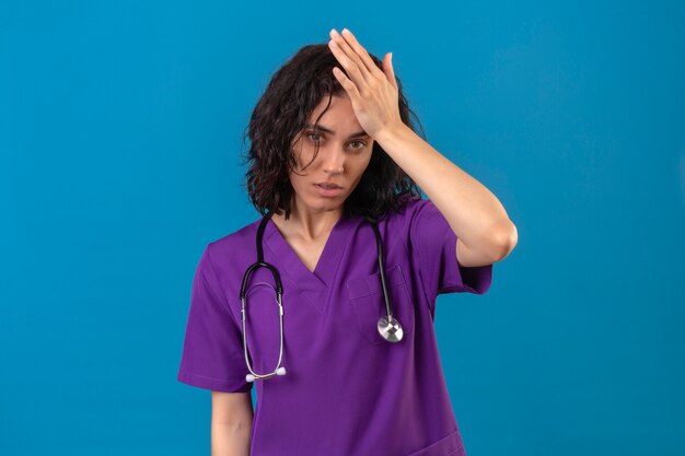 Jonge vrouw verpleegster in medisch uniform en met stethoscoop op zoek onzeker met twijfel denken met de hand op het hoofd staan