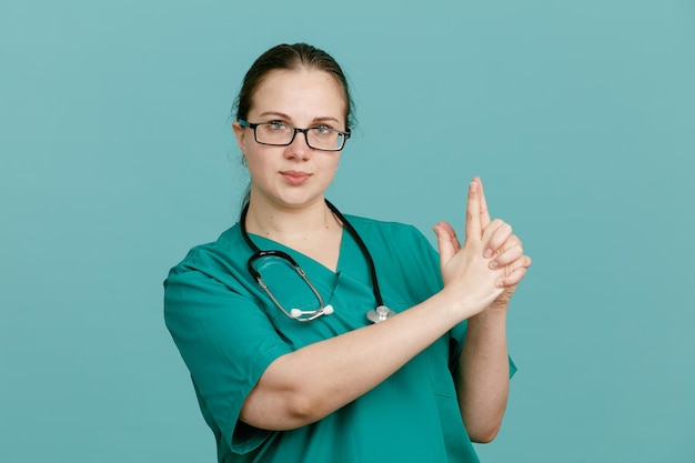 Jonge vrouw verpleegster in medisch uniform met stethoscoop om nek kijken camera met ernstige gezicht maken pistool gebaar pistool gebaar met handen permanent over blauwe achtergrond Premium Foto