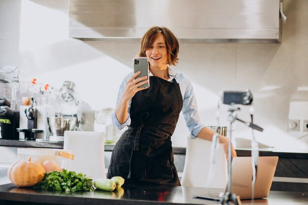 Jonge vrouw videoblogger koken in de keuken en filmen