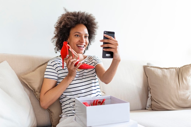 Jonge vrouw voelt zich opgewonden met nieuwe schoenen die aankopen uitpakt en thuis foto's maakt met de telefoon en ze op sociale media plaatst