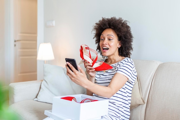 Jonge vrouw voelt zich opgewonden met nieuwe schoenen die aankopen uitpakt en thuis foto's maakt met de telefoon en ze op sociale media plaatst