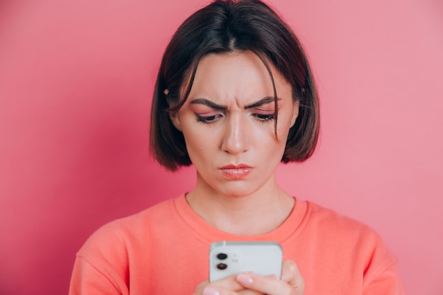 Jonge vrouw voelt zich verdrietig ongelukkig boos tijdens het lezen van sms met haar mobiele telefoon, op roze achtergrond