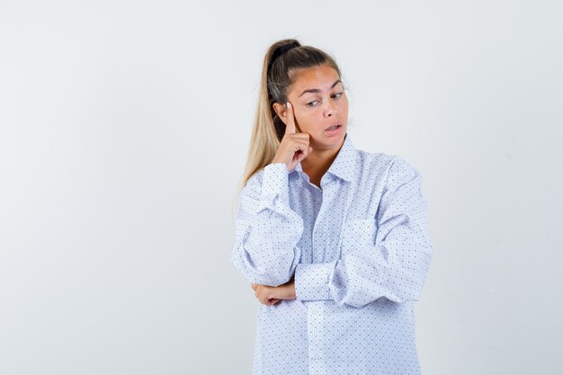 Jonge vrouw wang leunend op wijsvinger, iets in wit overhemd denken en peinzend kijken