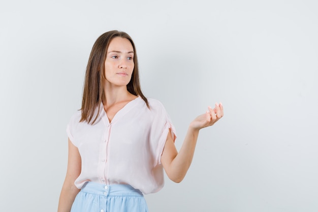 Jonge vrouw wegkijken met opgeheven palm in t-shirt, rok en peinzend, vooraanzicht kijken.