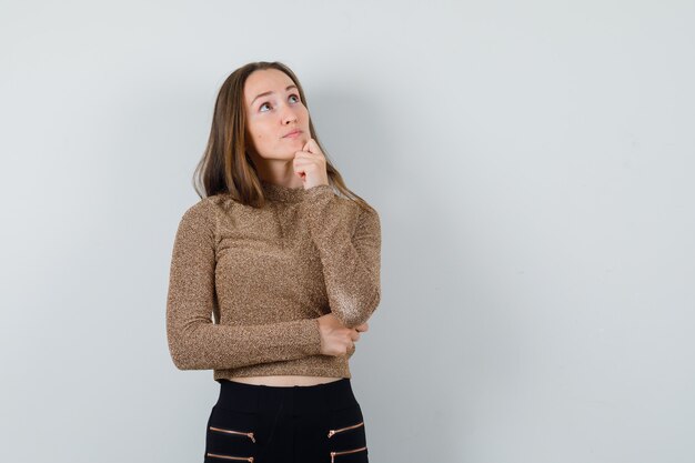 Jonge vrouw wegkijken terwijl denken in gouden blouse en nadenkend kijken