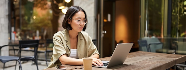 Gratis foto jonge vrouw werkt in een café met behulp van laptop en drinkt koffie aziatische studente met computer