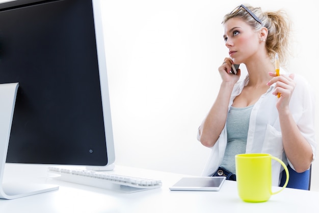 Jonge vrouw werkt thuis vanuit de computer en praten over de telefoon met het kantoor