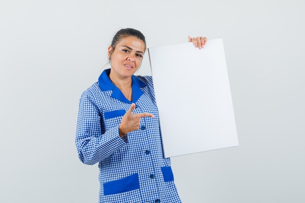 Jonge vrouw wijst naar blad in het blauwe overhemd van de gingangpyjama en ziet er mooi uit. vooraanzicht.