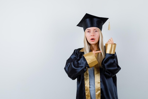 Jonge vrouw wijst naar haar mouw in afgestudeerd uniform en kijkt verrast