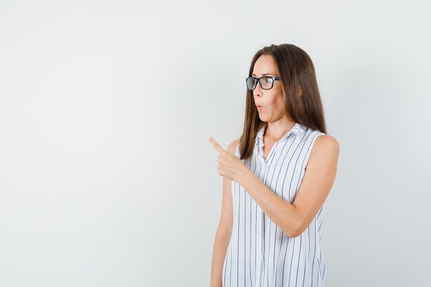 Jonge vrouw wijst weg in t-shirt en kijkt nieuwsgierig, vooraanzicht.