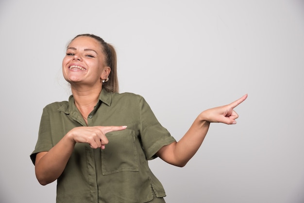 Jonge vrouw wijzend aan haar zijde op grijze muur.