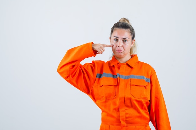 Jonge vrouw wijzend op haar tranen terwijl ze huilen in uniform van de werknemer en boos kijkt. vooraanzicht.