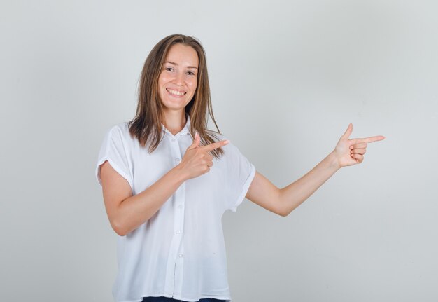 Jonge vrouw wijzende vingers naar de andere kant in wit t-shirt en op zoek vrolijk
