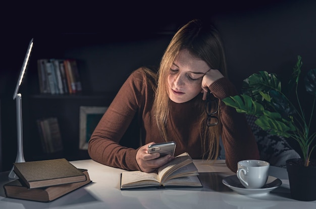 Jonge vrouw zit aan tafel en leest 's nachts een boek met een lamplicht