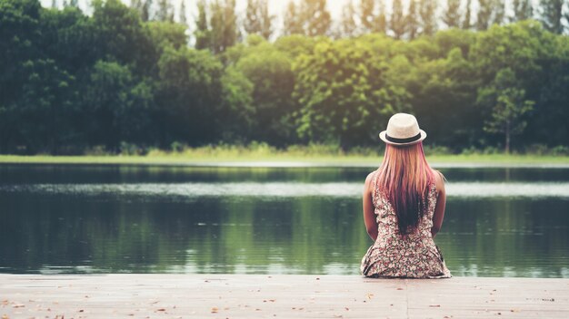 Jonge vrouw zit op de pier en kijkt naar de rivier.