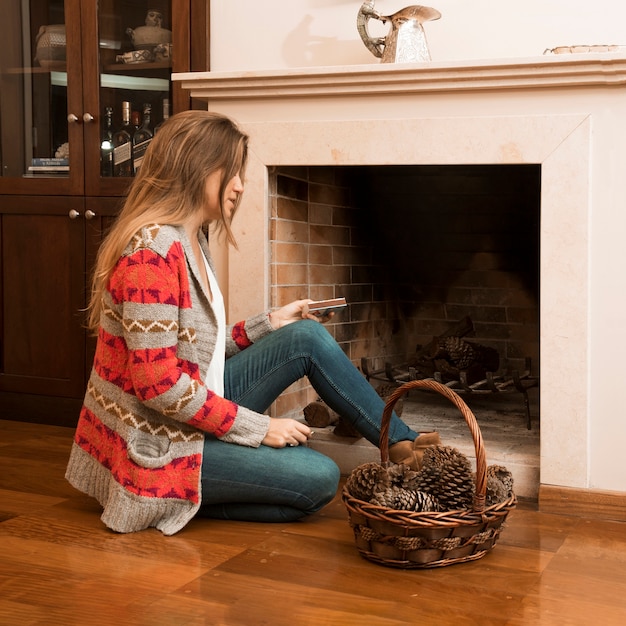 Jonge vrouw zitten buiten de open haard met matchbox en pinecone mand