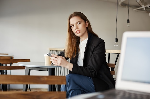 Jonge vrouw zitten in café met smartphone verward en op zoek naar iemand ondervraagd