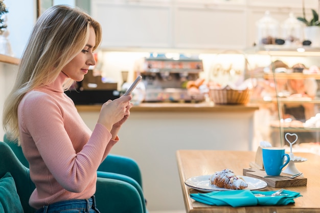 Jonge vrouw zitten in de caf� met behulp van de mobiele telefoon