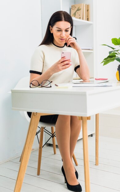 Jonge vrouw zittend aan tafel met smartphone