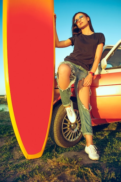 Jonge vrouw zittend op auto met surfplank