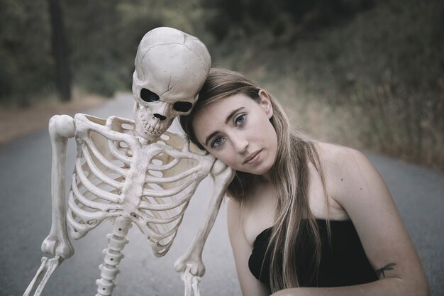 Jonge vrouw zittend op de weg met skelet