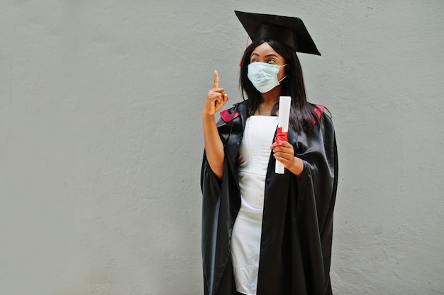 Jonge vrouwelijke afro-amerikaanse afgestudeerde student draagt een beschermend masker tegen coronavirus concept van afstudeerceremonie quarantaine